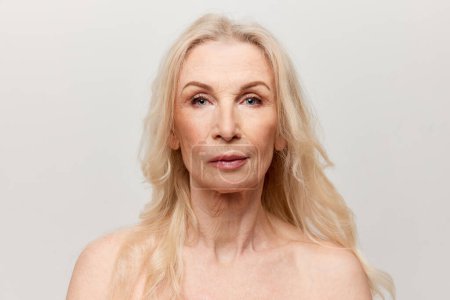 Téléchargez les photos : Portrait d'une belle femme d'âge moyen avec une peau saine et naturelle regardant la caméra sur fond de studio gris. Concept de beauté naturelle, soin de la peau du visage, cosmétologie et cosmétiques, santé - en image libre de droit