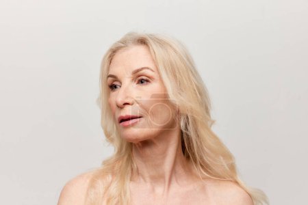 Téléchargez les photos : Portrait of beautiful middle-aged woman with well-kept healthy skin over grey studio background. Mature old lady. Concept of natural beauty, face skin care, cosmetology and cosmetics, health - en image libre de droit