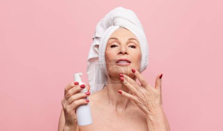 Téléchargez les photos : Deep cleaning. Beautiful middle-aged woman washing face with cleanser foam. Model posing over pink studio background. Concept of natural beauty, face skin care, cosmetology and cosmetics, health - en image libre de droit