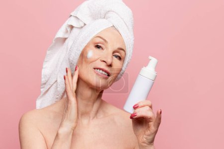 Foto de Beautiful middle-aged woman cleaning face with cleanser foam. Model posing over pink studio background. Concept of natural beauty, face skin care, cosmetology and cosmetics, health - Imagen libre de derechos