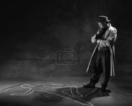 Foto de Black and white, noir photography. Thoughtful man, detective in hat and trench coat looking on human drawn silhouette on floor. Murder investigation. Occupation, character, history. Retro style - Imagen libre de derechos