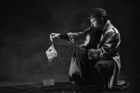 Téléchargez les photos : Photographie noir et blanc, noir. Inspecteur assis près d'une silhouette dessinée par des humains, regardant un mouchoir avec des taches de sang dans une loupe. Occupation, caractère, histoire. Style rétro - en image libre de droit