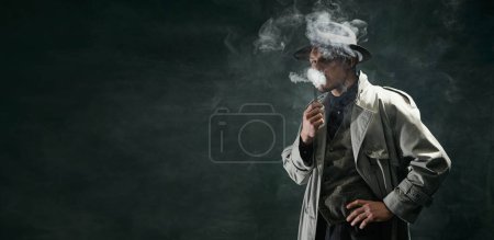 Téléchargez les photos : Portrait of man, detective in trench coat and hat smoking pipe over vintage dark green background. Banner. Concept of occupation, character, history. Retro style. Copy space for ad - en image libre de droit
