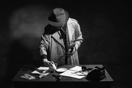 Photo for Black and white, noir photography. Man, professional detective, inspector in trench coat looking through clues of case, cup, handkerchief. Concept of occupation, character, history. Retro style - Royalty Free Image