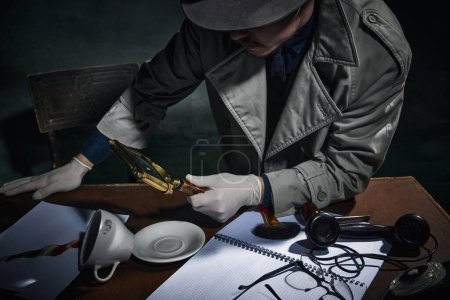 Foto de Cropped image of male detective looking in magnifying glass at fingerprints on coffee cup, finding case clues. Professional investigation. Concept of occupation, character, history. Retro style - Imagen libre de derechos
