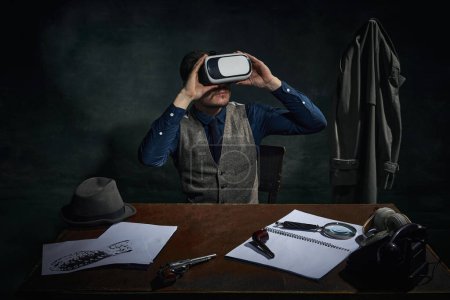 Téléchargez les photos : Professional detective in classical clothes and virtual reality glasses over dark green vintage background. Investigation. Modern technologies. Concept of occupation, character, history. Retro style - en image libre de droit