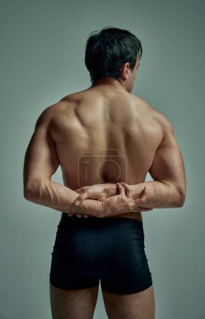 Foto de Rear view of strong muscular relief males back. Handsome young model posing in black underwear over studio background. Concept of mans beauty, sportive and healthy lifestyle, fashion - Imagen libre de derechos