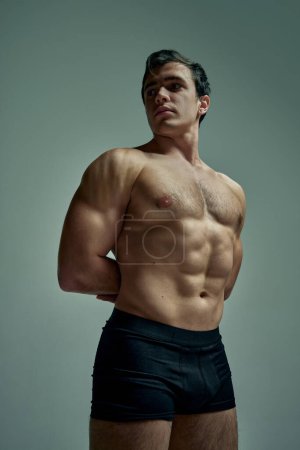 Téléchargez les photos : Relief body shape. Handsome young man with muscular body posing shirtless in black underwear over studio background. Concept of mans beauty, sportive and healthy lifestyle, fashion - en image libre de droit