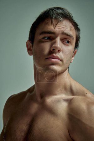 Téléchargez les photos : Relief body. Portrait of handsome young man with muscular body posing shirtless over pale green over studio background. Concept of mans beauty, sportive and healthy lifestyle, fashion - en image libre de droit