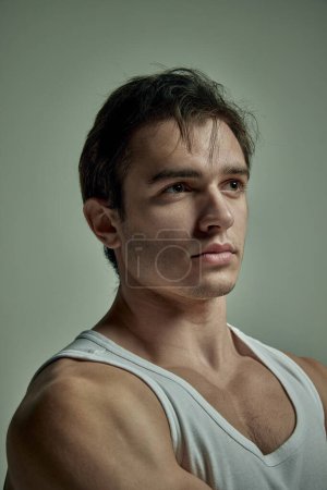 Photo for Portrait of serious handsome young man with muscular body posing in singlet over pale green studio background. Concept of mans beauty, sportive and healthy lifestyle, fashion - Royalty Free Image