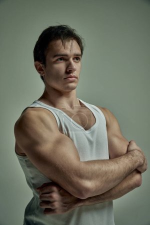 Photo for Strong muscular hands. Portrait of serious handsome young man with muscular body posing in singlet over pale green studio background. Concept of mans beauty, sportive and healthy lifestyle, fashion - Royalty Free Image