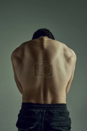Photo for Round back. Male strong healthy back. Model posing shirtless over pale green studio background. Muscular body shape. Concept of mans beauty, sportive and healthy lifestyle, fashion - Royalty Free Image