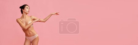 Téléchargez les photos : Belle jeune fille avec une forme de corps mince posant en sous-vêtements sur fond de studio rose. Concept de beauté naturelle, fitness, alimentation, soins du corps, sport et santé. Bannière. Espace timide pour la publicité - en image libre de droit