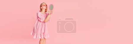 Téléchargez les photos : Beauty as it is. Young tender girl in pink dress looking at mirror over pink studio background. Concept of beauty, emotions, fashion, lifestyle and youth culture. Banner. Copy space for ad - en image libre de droit