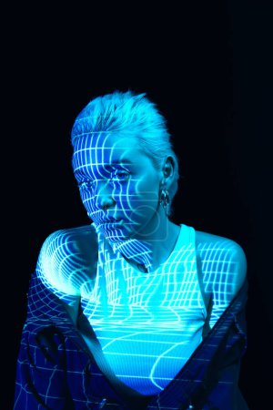 Foto de Abstracción e ilusión. Retrato de una joven rubia con rayas de neón en la cara posando sobre fondo oscuro en luces de neón azules. Concepto de arte, estilo moderno, cyberpunk, futurismo y creatividad - Imagen libre de derechos