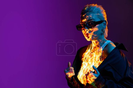 Téléchargez les photos : Surréalisme. Portrait de jeune fille blonde avec feu brûlant numérique sur le corps posant sur fond violet dans des néons bleus. Concept d'art, style moderne, cyberpunk, futurisme et créativité - en image libre de droit
