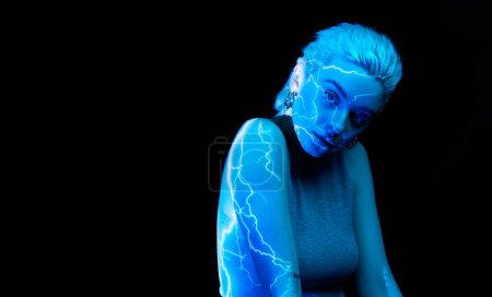 Téléchargez les photos : Éclaircissement. Portrait de jeune fille blonde avec des rayures abstraites au néon sur le corps posant sur un fond sombre dans des néons bleus. Concept d'art, style moderne, cyberpunk, futurisme et créativité - en image libre de droit
