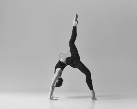 Téléchargez les photos : Black and white photography. Young flexible sportive girl doing stretching exercises, training over studio background. Concept of sport, body care, beauty, fitness, active lifestyle. Ad - en image libre de droit