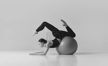 Téléchargez les photos : Fitness aesthetics. Black and white photography. Young sportive girl training with fitness ball, balancing over studio background. Concept of sport, body care, beauty, fitness, active lifestyle. Ad - en image libre de droit