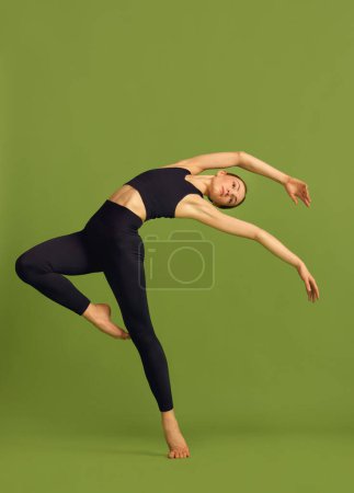 Foto de Graceful movements. Young slim sportive girl doing stretching, training over green studio background. Concept of sport, art, body care, beauty, fitness, active lifestyle and health. Ad - Imagen libre de derechos