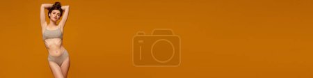 Foto de Mujer hermosa joven posando en ropa interior gris sobre fondo de estudio naranja. Forma de cuerpo delgado. Concepto de belleza, fitness, spa, cosmetología, cuidado de la piel y del cuerpo. Banner. Copiar espacio para anuncio - Imagen libre de derechos