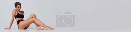 Photo for Beautiful young woman with slim fit body posing in black underwear over grey studio background. Concept of body and skin care, fitness, health, wellness. Banner, flyer. Copy space for ad - Royalty Free Image