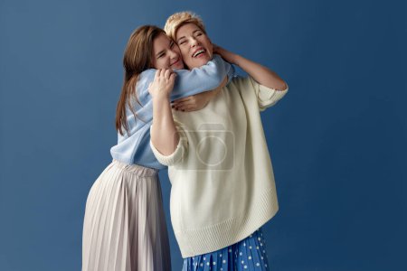Foto de Endless love. Portrait of happy middle-aged woman and her young daughter hugging, posing over blue studio background. Concept of motherhood, family, mothers day, love, emotions, relationship - Imagen libre de derechos
