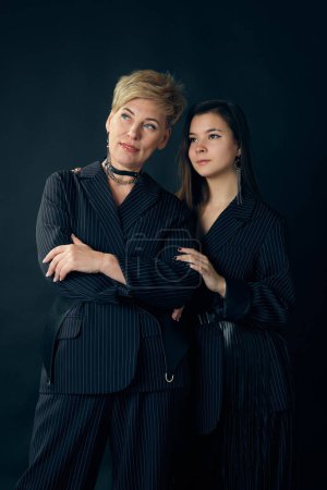 Foto de Relatives bond. Beautiful middle aged woman, mother with her young daughter posing over dark studio background. Concept of motherhood, family, mothers day, love, emotions, relationship - Imagen libre de derechos