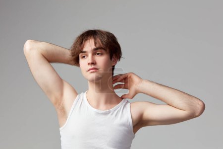 Foto de Studio portrait of young man with well-kept skin posing in singlet against grey background. Concept of mens health, body and skin care, hygiene and male cosmetology - Imagen libre de derechos