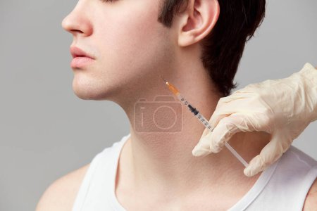 Foto de Chin fillers. Cropped image of young man doing cosmetological injections. Male model against grey studio background. Concept of mens health, skin care, hygiene and male cosmetological treatment - Imagen libre de derechos