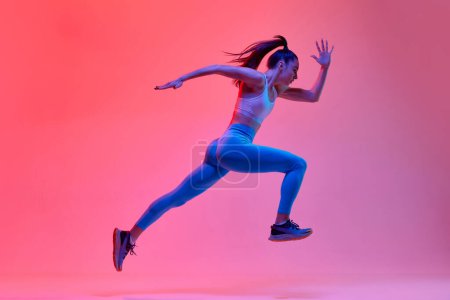 Photo for Dynamic portrait of young active girl, athlete, runner in motion, training over pink studio background in neon light. Concept of sportive lifestyle, health, endurance, action and motion. Ad - Royalty Free Image