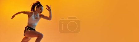 Téléchargez les photos : Dynamic image of young sportive girl, professional runner training over orange studio background in neon light. Concept of sportive lifestyle, health, endurance, motion. Banner. Copy space for ad - en image libre de droit