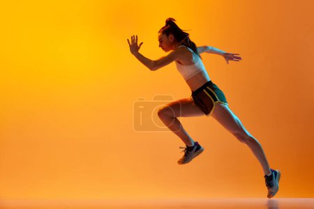 Téléchargez les photos : Dynamic image of professional female runner, athlete in motion, running over orange studio background in neon light. Concept of sportive lifestyle, health, competition, endurance, action. Ad - en image libre de droit