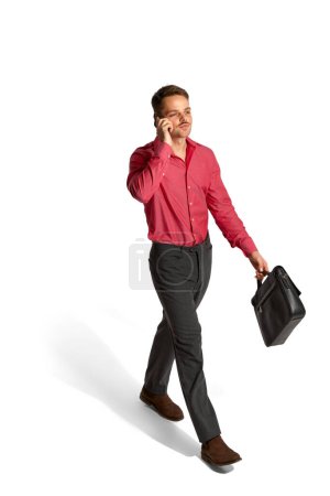Photo for Young employee, man in official clothes talking on phone on his way, posing over white studio background. Isometric view. Concept of career development, employment, business, job. Ad - Royalty Free Image