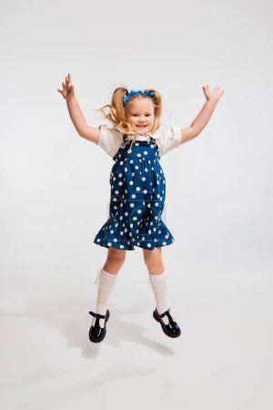 Photo for Beautiful cute little girl, child in retro style dress jumping, posing against grey studio background. Concept of childhood, game, emotions, activity, leisure time, retro style, fashion. - Royalty Free Image