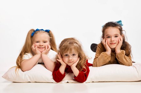 Photo pour Relaxation and fun. Cute little beautiful girls, kids lying on big pillow against grey studio background. Concept of childhood, game, friendship, activity, leisure time, retro style, fashion. - image libre de droit