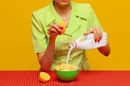 Téléchargez les photos : Image recadrée d'une femme en costume rétro mettant du lait et pressant du jus de citron dans des céréales sur fond de studio rose. Photographie pop art culinaire. Couleurs complémentaires. Espace de copie pour annonce, texte - en image libre de droit
