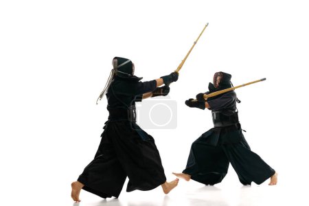 Téléchargez les photos : Deux hommes, des athlètes professionnels de kendo en mouvement, se battant, s'entraînant avec l'épée de bambou shinai sur fond de studio blanc. Concept d'arts martiaux, sport, culture japonaise, action - en image libre de droit