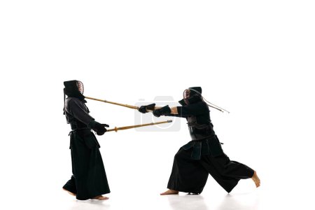 Men, professional kendo athletes in uniform raining with shinai sword against white studio background. Winner. Concept of martial arts, sport, Japanese culture, action and motion, strength