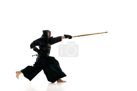 Téléchargez les photos : Homme, athlète kendo professionnel en uniforme noir avec épée, entraînement shinai sur fond de studio blanc. Concept d'arts martiaux, sport, culture japonaise, action et mouvement, pouvoir - en image libre de droit