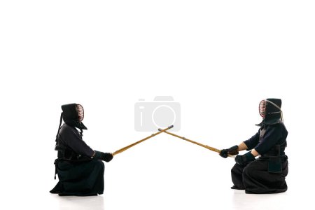 Téléchargez les photos : Début du combat. Deux hommes, athlètes professionnels de kendo en uniforme avec casque avec épée en bambou shinai sur fond de studio blanc. Concept d'arts martiaux, sport, culture japonaise, action, mouvement - en image libre de droit