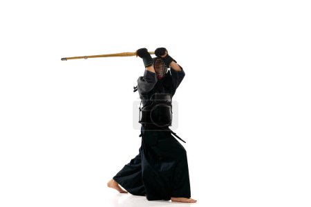 Foto de Retrato de hombre, atleta kendo profesional en pose uniforme, entrenamiento con espada shinai sobre fondo blanco del estudio. Concepto de artes marciales, deporte, cultura japonesa, acción y movimiento - Imagen libre de derechos