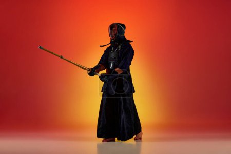 Photo for Full-length portrait of man, professional kendo athlete in uniform posing with shinai sword against gradient studio background in neon light. Concept of martial arts, sport, Japanese culture, motion - Royalty Free Image
