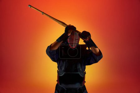 Téléchargez les photos : Vue de face. Portrait d'homme, athlète kendo professionnel en uniforme posant avec épée shinai contre fond de studio dégradé au néon. Concept d'arts martiaux, sport, culture japonaise, mouvement - en image libre de droit