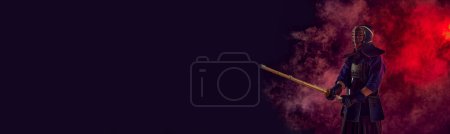 Photo for Man, professional kendo athlete, combat sportsman posing with shinai sword against gradient dark background in neon light with smoke. Concept of martial arts, sport, Japanese culture. Banner - Royalty Free Image