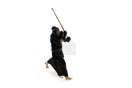 Téléchargez les photos : Vue de dessus. Homme, athlète professionnel de kendo en uniforme avec entraînement de casque avec épée en bambou shinai sur fond de studio blanc. Concept d'arts martiaux, sport, culture japonaise, action et mouvement - en image libre de droit
