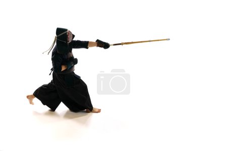 Foto de Hombre, atleta kendo profesional en uniforme con entrenamiento de casco con espada shinai de bambú sobre fondo de estudio blanco. Concepto de artes marciales, deporte, cultura japonesa, acción y movimiento - Imagen libre de derechos