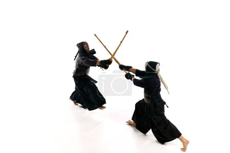 Téléchargez les photos : Vue de dessus. Image dynamique de deux hommes, athlètes professionnels de kendo en uniforme d'entraînement avec épée shinai sur fond de studio blanc. Concept d'arts martiaux, sport, culture japonaise, action, mouvement - en image libre de droit