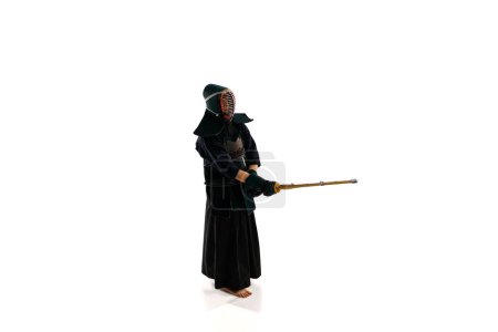 Téléchargez les photos : Vue de dessus. Homme, athlète professionnel de kendo en uniforme avec casque posant avec épée de bambou shinai sur fond de studio blanc. Concept d'arts martiaux, sport, culture japonaise, action et mouvement - en image libre de droit