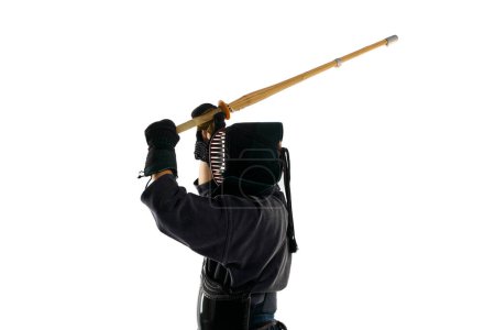 Foto de Vista superior. Hombre, atleta kendo profesional en uniforme con entrenamiento de casco con espada shinai de bambú sobre fondo de estudio blanco. Concepto de artes marciales, deporte, cultura japonesa, acción y movimiento - Imagen libre de derechos